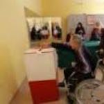 osoba niepełnopsrawna na wózku wrzuca kartę do głosowania do urny wyborczej